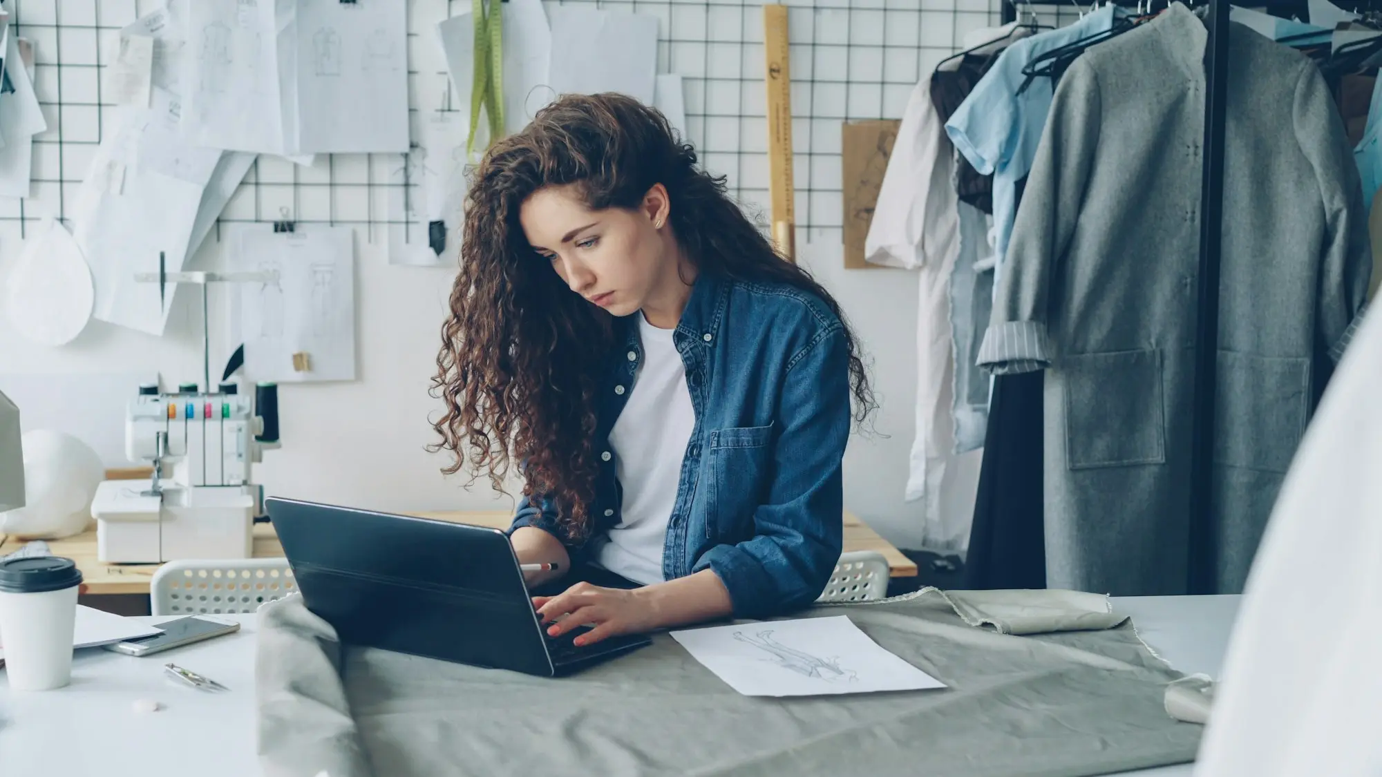 Fashion maker checking a loan approval on her laptop in the workshop